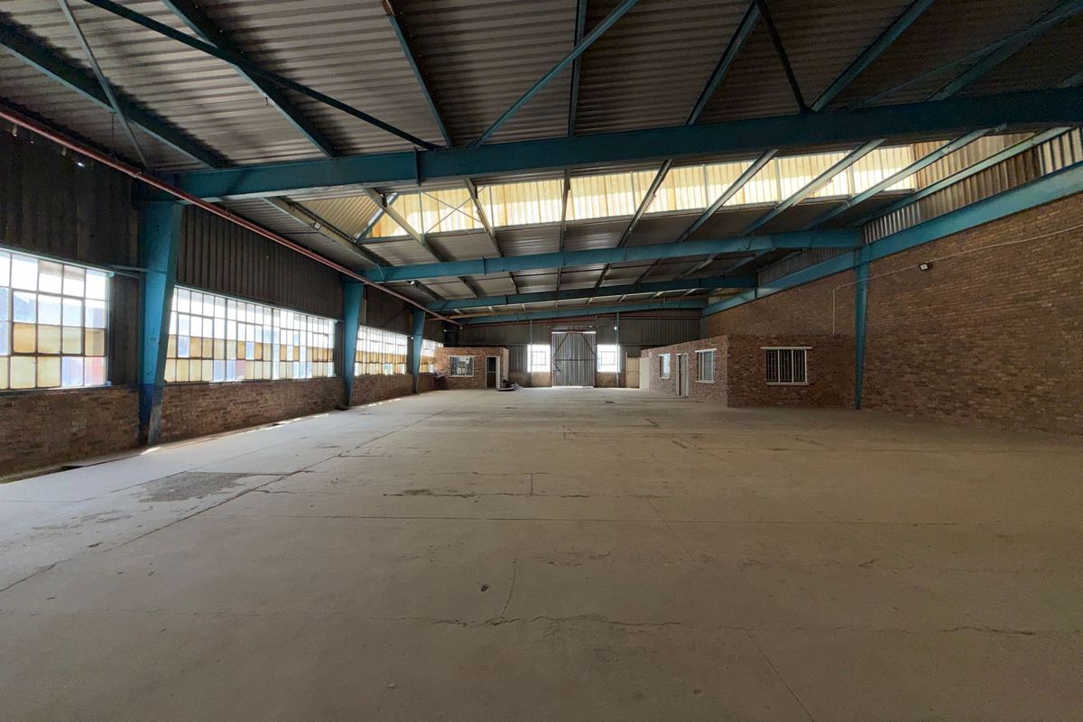 Spacious industrial warehouse featuring high ceilings with exposed steel trusses, concrete flooring, and large steel-framed windows providing ample natural light.