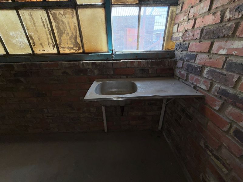 A basic industrial utility space featuring an exposed brick wall, a stainless steel sink, and aged steel-framed windows.