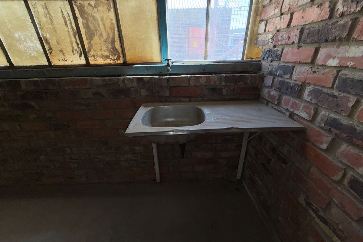 A basic industrial utility space featuring an exposed brick wall, a stainless steel sink, and aged steel-framed windows.