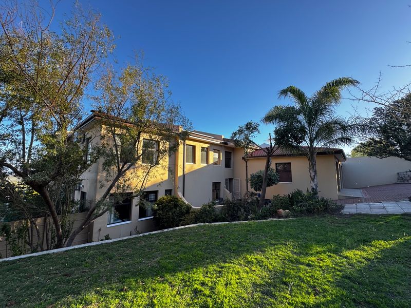 Rear view of a two-story residential property featuring plastered walls, terracotta roof tiles, and a landscaped garden area with a paved driveway.