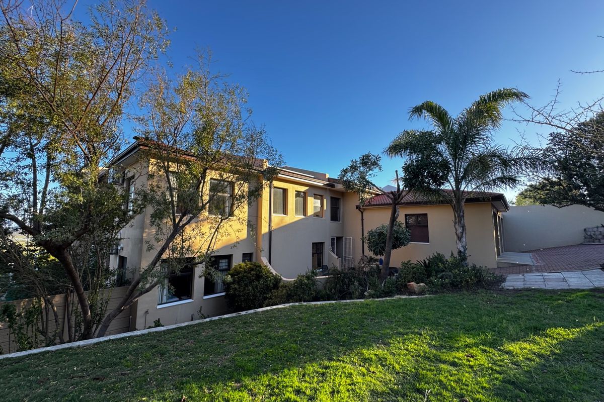 Rear view of a two-story residential property featuring plastered walls, terracotta roof tiles, and a landscaped garden area with a paved driveway.