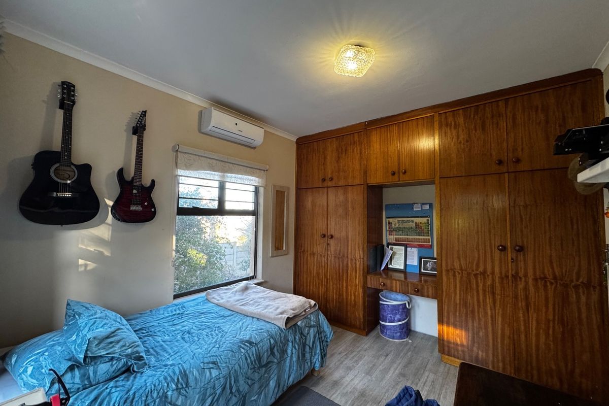 A bedroom featuring extensive built-in wooden cabinetry with an integrated desk area, a split-system air conditioner, and laminate flooring.
