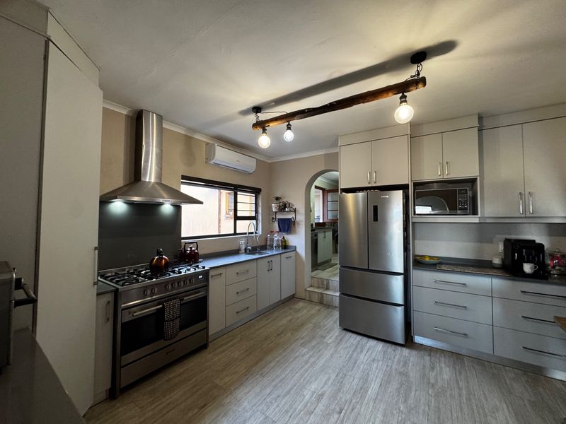 Modern kitchen featuring stainless steel appliances, gas stove, extractor fan, ample cabinetry, and laminate flooring with an adjacent scullery area.