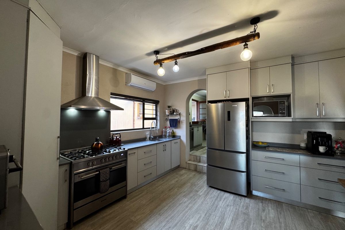 Modern kitchen featuring stainless steel appliances, gas stove, extractor fan, ample cabinetry, and laminate flooring with an adjacent scullery area.