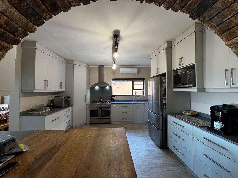 Modern kitchen featuring light-toned cabinetry, stone countertops, stainless steel appliances, and a distinctive brick archway entrance.