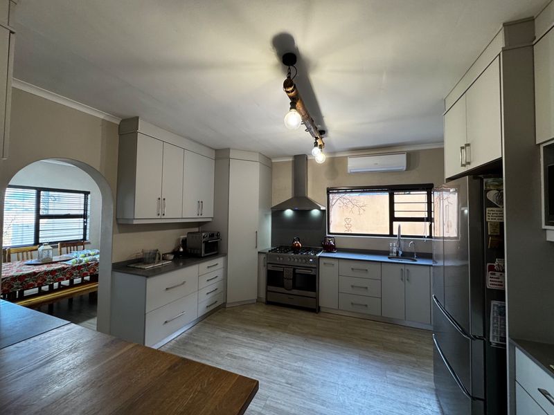 Modern kitchen featuring light-toned cabinetry, stainless steel appliances, gas stove, extractor fan, and tiled flooring, with an open archway leading to the dining area.