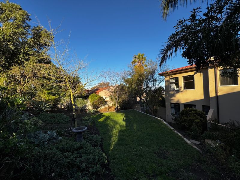 A well-maintained rear garden featuring a manicured lawn and established landscaping, adjacent to the side elevation of the double-story residential property.