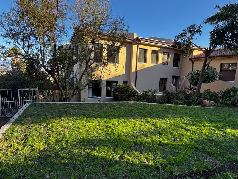 Rear view of the multi-story residential property featuring a well-maintained lawn and established garden area.