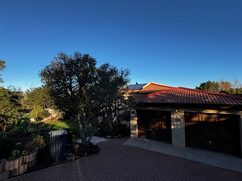 Front view of the property featuring a double garage, paved driveway, and a tiled roof equipped with solar panels.