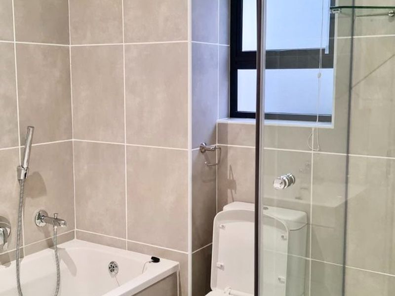 Modern bathroom featuring a tiled bathtub, separate glass-enclosed shower, and toilet with neutral wall and floor tiling.