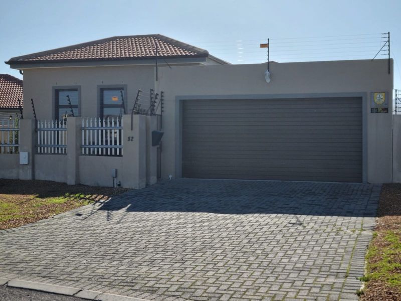 Front elevation of a modern house featuring a paved driveway, automated garage door, and secure boundary wall with electric fencing.