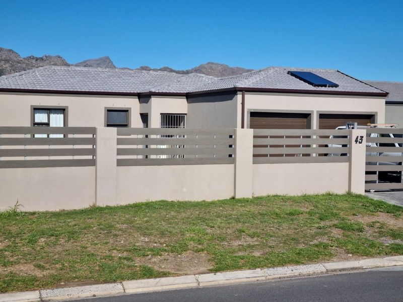 Front elevation of a modern house featuring a double garage, solar water heating panel, and a secure perimeter wall with slatted fencing.