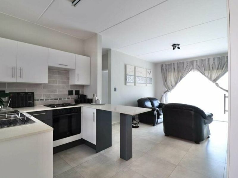 Modern open-plan kitchen and living area featuring sleek cabinetry, stone countertops, built-in appliances, and neutral tiled flooring throughout.