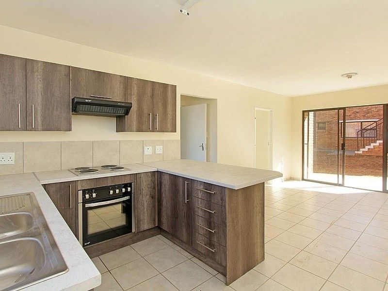 Open-plan kitchen featuring modern wood-look cabinetry, built-in oven and hob, and tiled flooring, flowing into a bright living area with sliding door access.