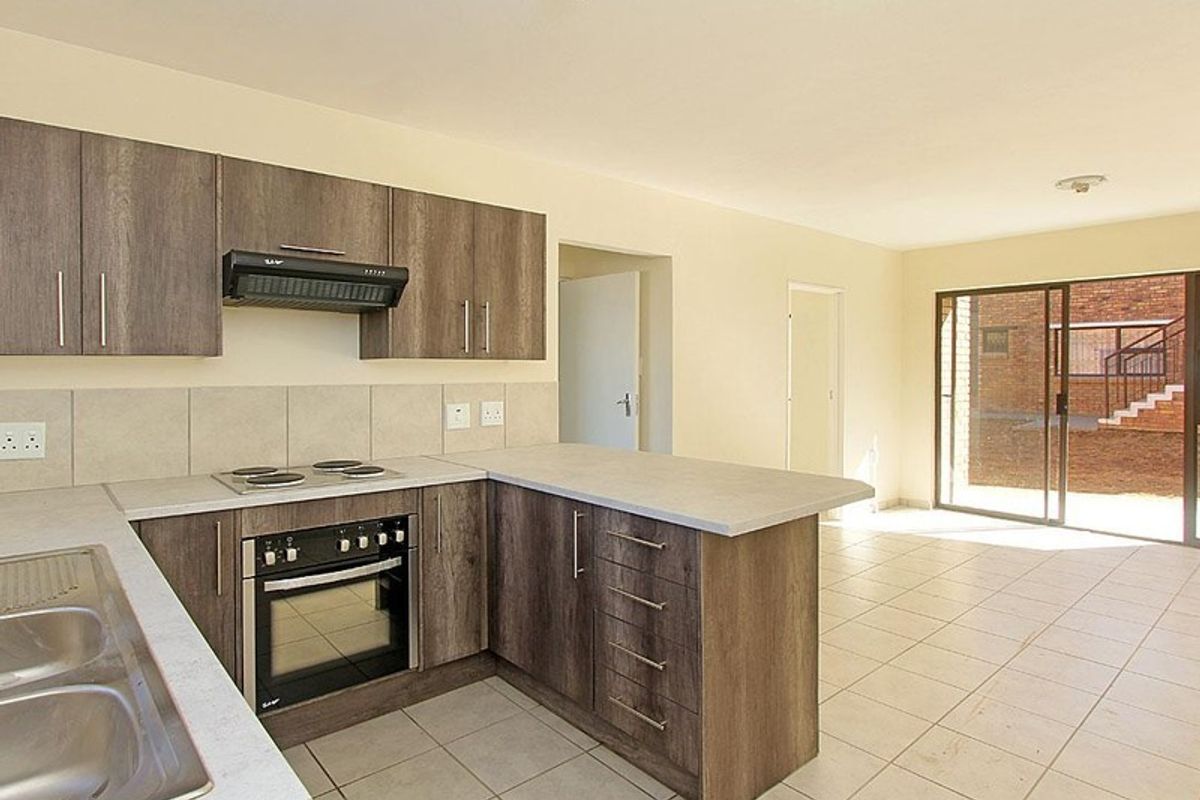 Open-plan kitchen featuring modern wood-look cabinetry, built-in oven and hob, and tiled flooring, flowing into a bright living area with sliding door access.