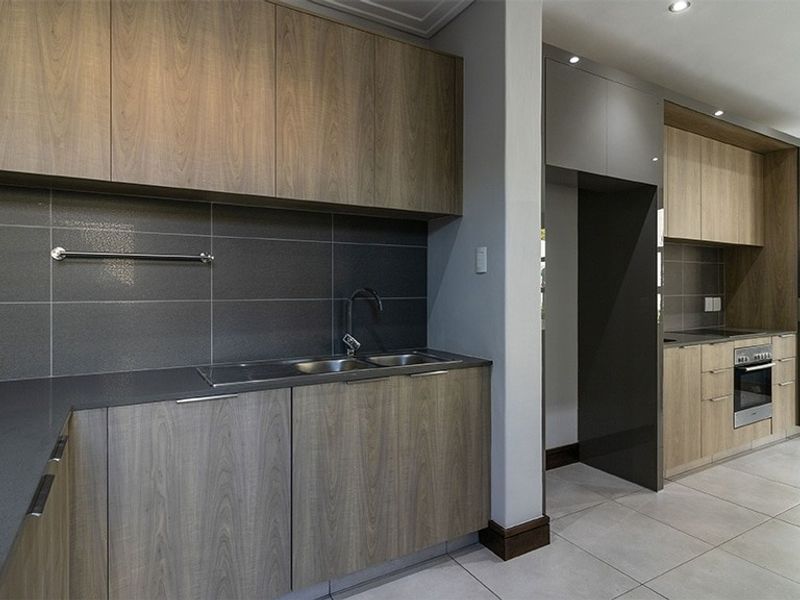 Modern kitchen featuring wood-grain cabinetry, dark stone countertops, tiled backsplash, integrated oven, and sleek recessed lighting in a clean, contemporary layout.