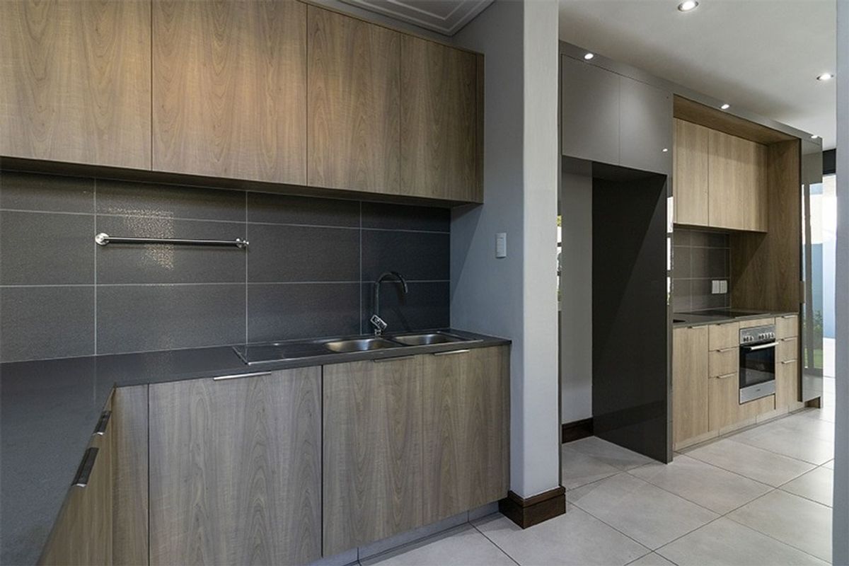 Modern kitchen featuring wood-grain cabinetry, dark stone countertops, tiled backsplash, integrated oven, and sleek recessed lighting in a clean, contemporary layout.
