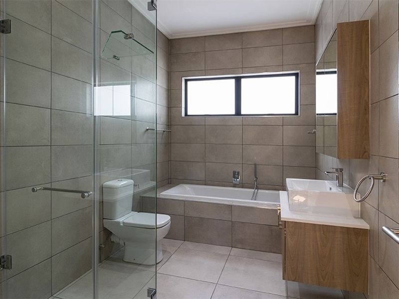 Modern bathroom featuring a glass-enclosed shower, built-in bathtub, wall-mounted vanity with basin, and neutral ceramic tiling throughout.