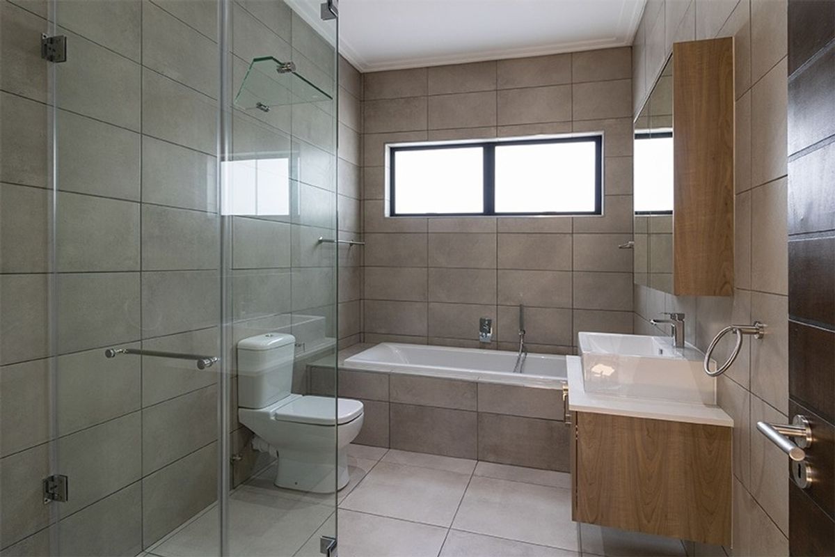Modern bathroom featuring a glass-enclosed shower, built-in bathtub, wall-mounted vanity with basin, and neutral ceramic tiling throughout.
