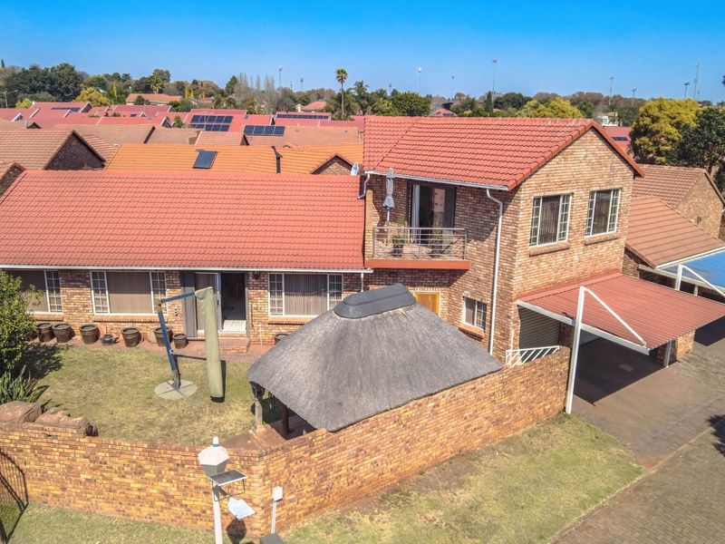 Aerial view of a brick townhouse featuring a tiled roof, a private balcony, a thatched lapa, and a covered carport within a residential complex.