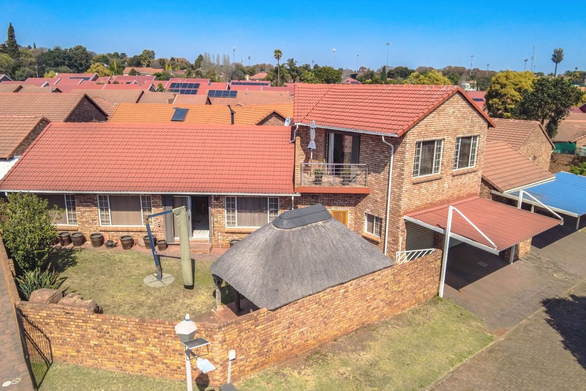 Aerial view of a brick townhouse featuring a tiled roof, a private balcony, a thatched lapa, and a covered carport within a residential complex.
