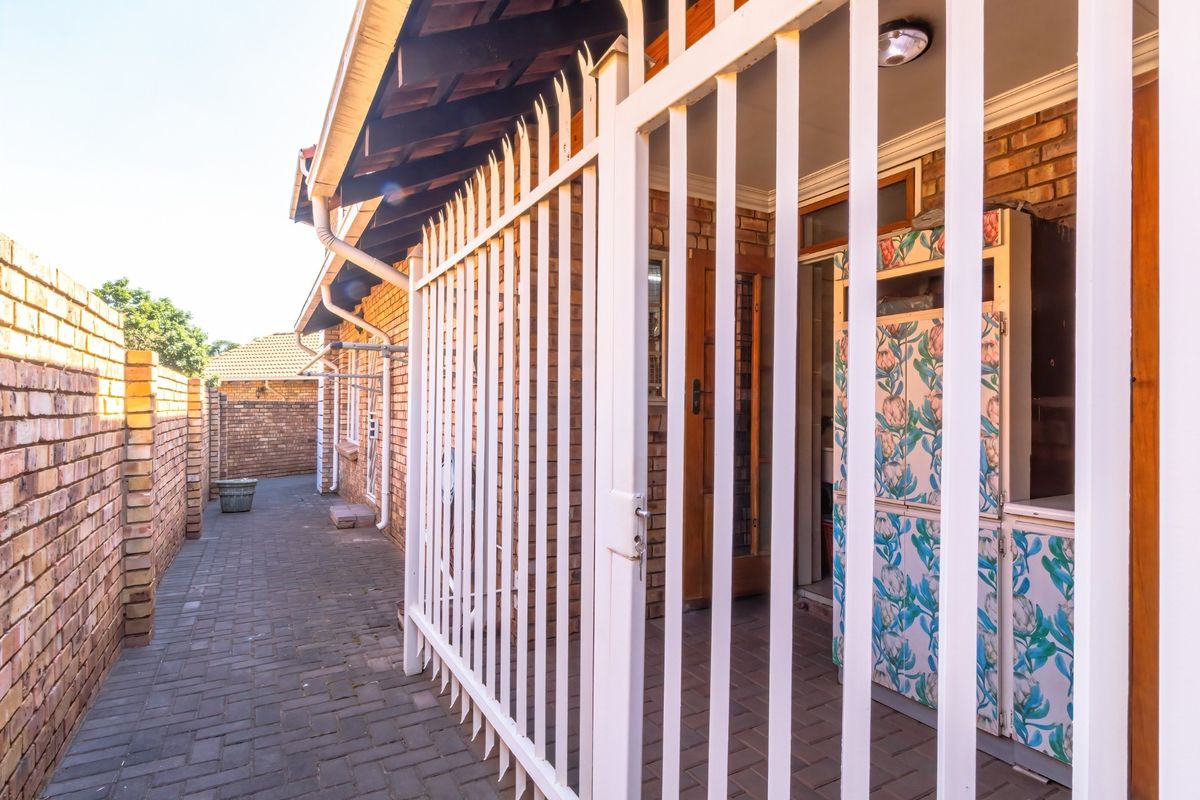 A side walkway of the townhouse featuring brick boundary walls, paved flooring, and a secure gated entrance with exposed timber roof rafters.