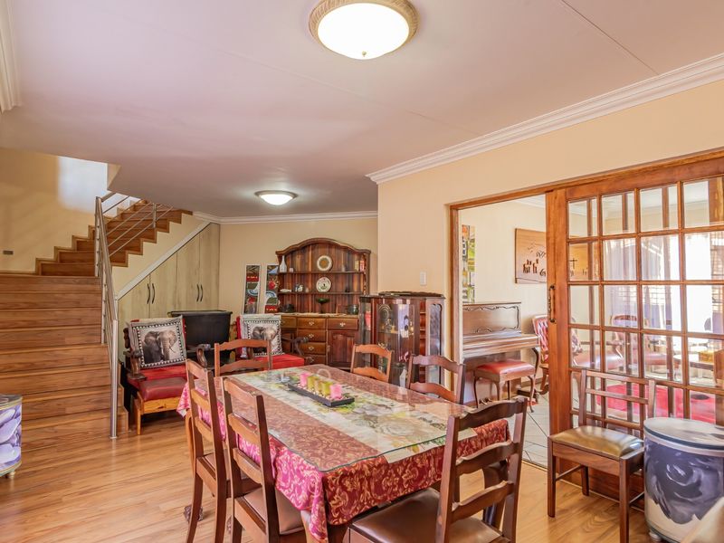 Dining area featuring laminate flooring, crown molding, and a wooden staircase with a stainless steel balustrade, leading to an adjacent room via sliding doors.