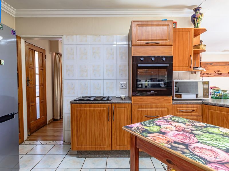 A functional kitchen featuring wood-look laminate cabinetry, built-in oven, electric hob, tiled backsplash, and tiled flooring, offering a traditional layout.