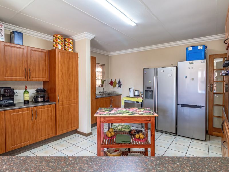 A functional kitchen featuring wood-look laminate cabinetry, tiled flooring, and a double sink, offering a practical layout with ample storage space.