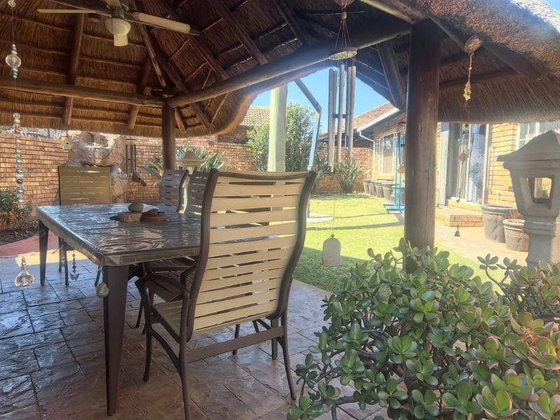 A covered outdoor patio area featuring a traditional thatched roof, timber support posts, and stamped concrete flooring, overlooking a private garden space.