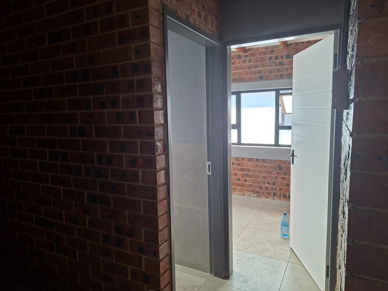 A view through an open doorway into an adjacent space featuring exposed brick walls, tiled flooring, and an aluminium window frame.