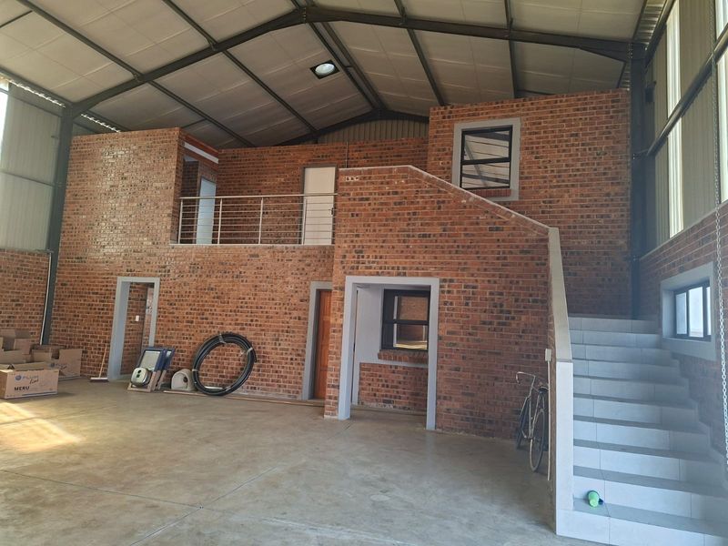 Spacious industrial open-plan area featuring exposed brickwork, a mezzanine level with a metal staircase, and high-clearance industrial roofing.