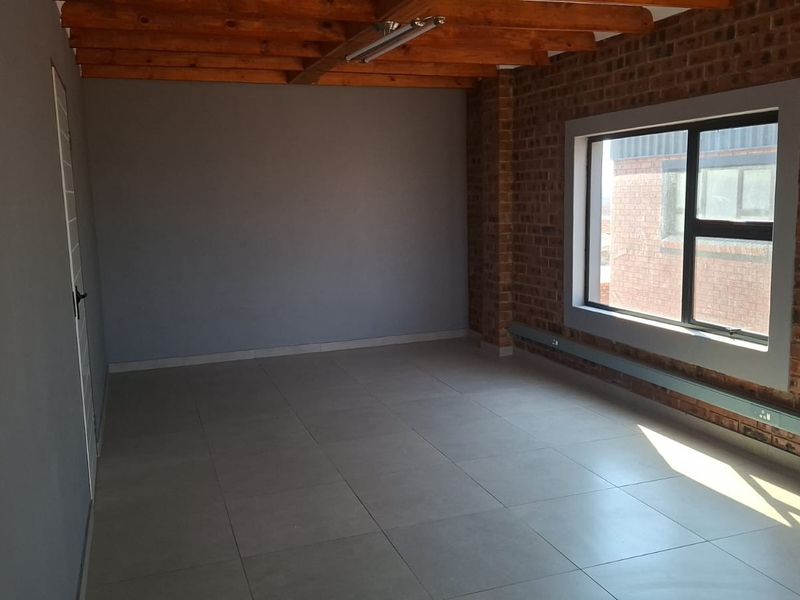 A bright, empty office space featuring exposed timber ceiling beams, an exposed brick feature wall, and modern tiled flooring.