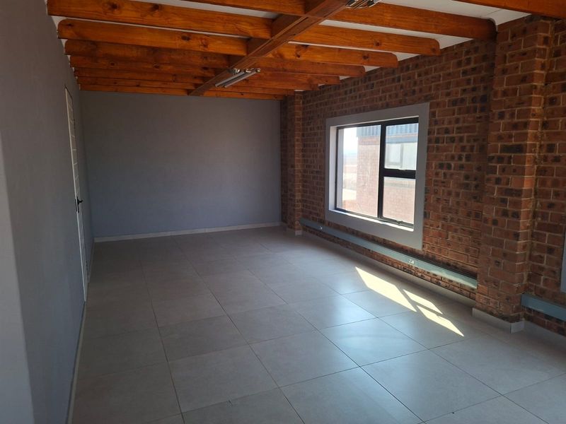 A bright, empty office space featuring exposed timber ceiling beams, a rustic brick feature wall, and modern tiled flooring.