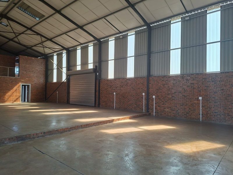 Spacious industrial warehouse unit featuring exposed brick walls, polished concrete flooring, a large roller shutter door, and a mezzanine level for additional storage or office space.
