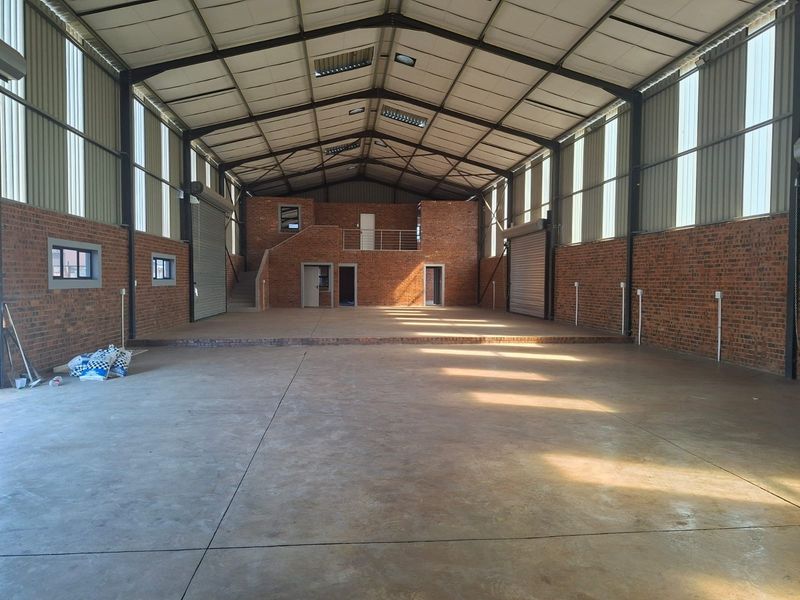 Spacious industrial warehouse featuring exposed brick walls, concrete flooring, a mezzanine level, and large roller shutter doors, providing versatile open-plan utility space.