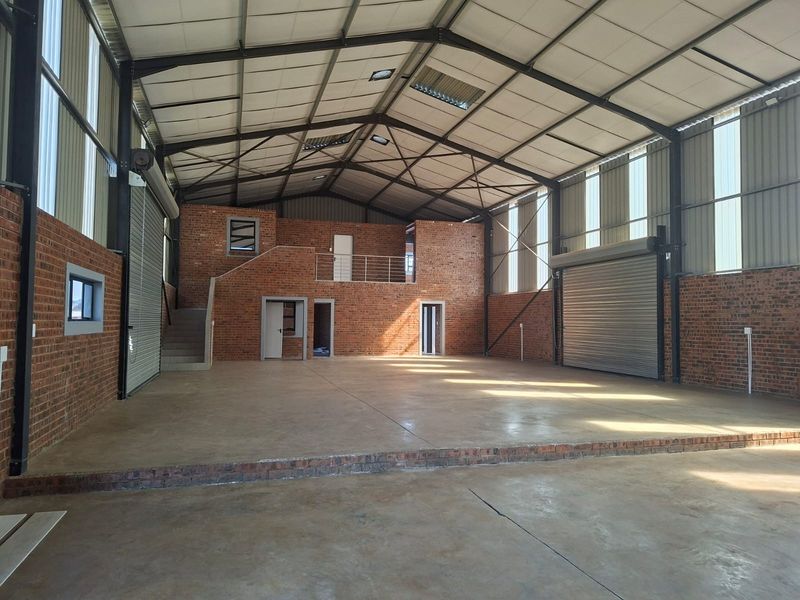 Spacious industrial warehouse featuring exposed brick walls, concrete flooring, high-clearance steel portal frame, roller shutter doors, and a functional mezzanine level.