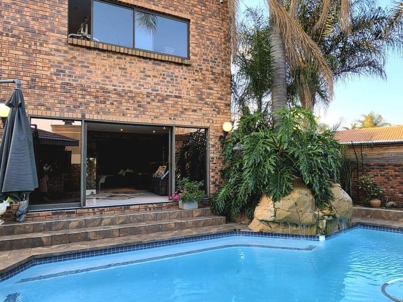 A well-maintained backyard featuring a swimming pool, brick exterior facade, and large sliding glass doors leading into the home.