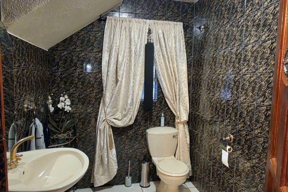 A compact bathroom featuring dark marble-effect wall tiles, a white pedestal basin, and a standard toilet under a sloped ceiling.
