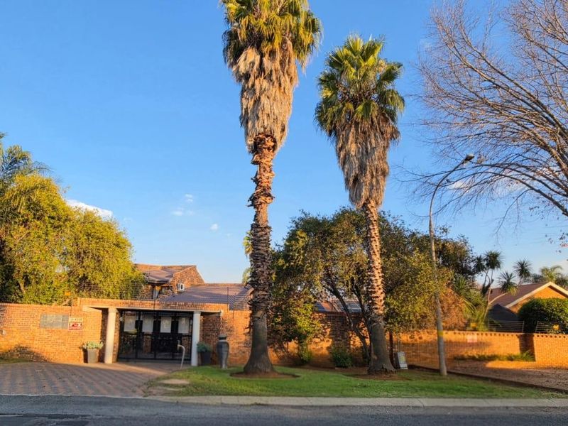 Front exterior view of the property featuring a brick boundary wall, paved driveway, and secure gated entrance with mature landscaping.