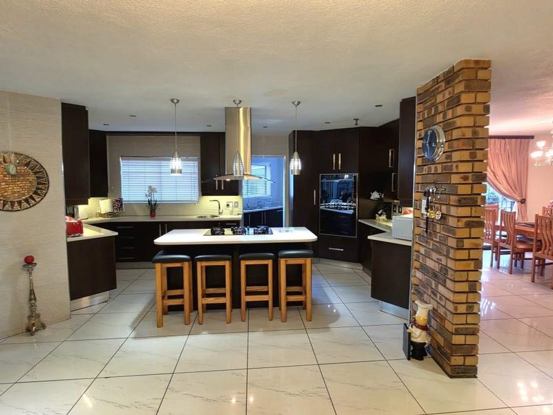 Spacious open-plan kitchen featuring a central island with hob, dark cabinetry, and tiled flooring, seamlessly flowing into the adjacent dining area.