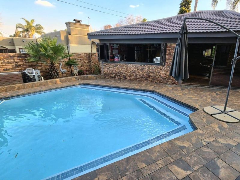 Outdoor pool area featuring a tiled surround, brick boundary wall, and a structure with bi-fold windows opening onto the pool deck.