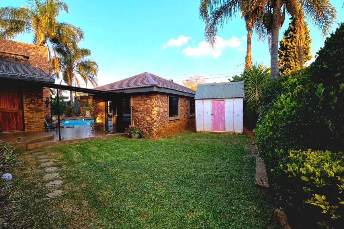 A spacious rear garden featuring a brick-built home, a covered patio area, a swimming pool, and a detached garden shed.