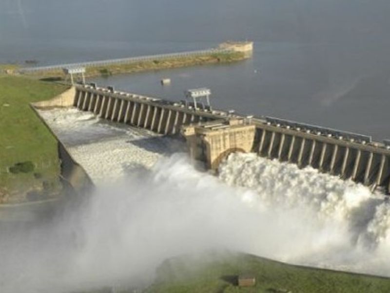 An aerial view of a large dam structure with water discharging through the spillway into the river below.