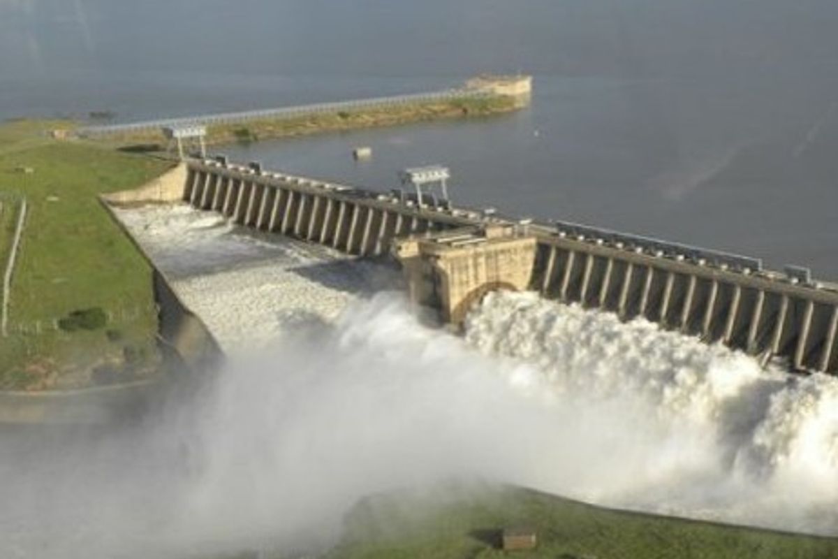 An aerial view of a large dam structure with water discharging through the spillway into the river below.