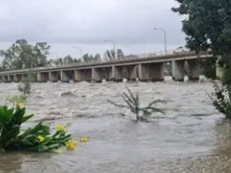 A view of a bridge over a flooded river, showing significant water levels and environmental conditions affecting the property area.