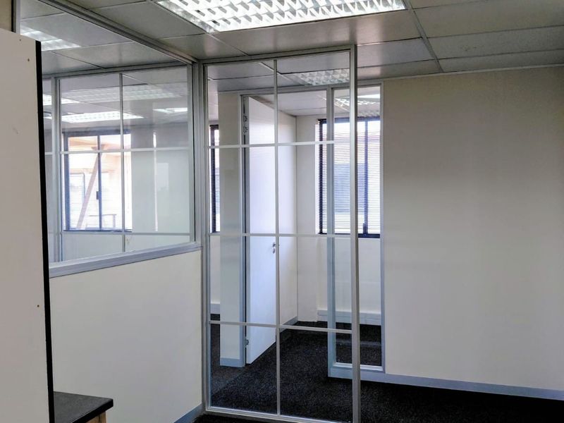A clean, vacant office space featuring glass partition walls, suspended ceilings with recessed lighting, and dark carpeting, offering a professional and functional work environment.