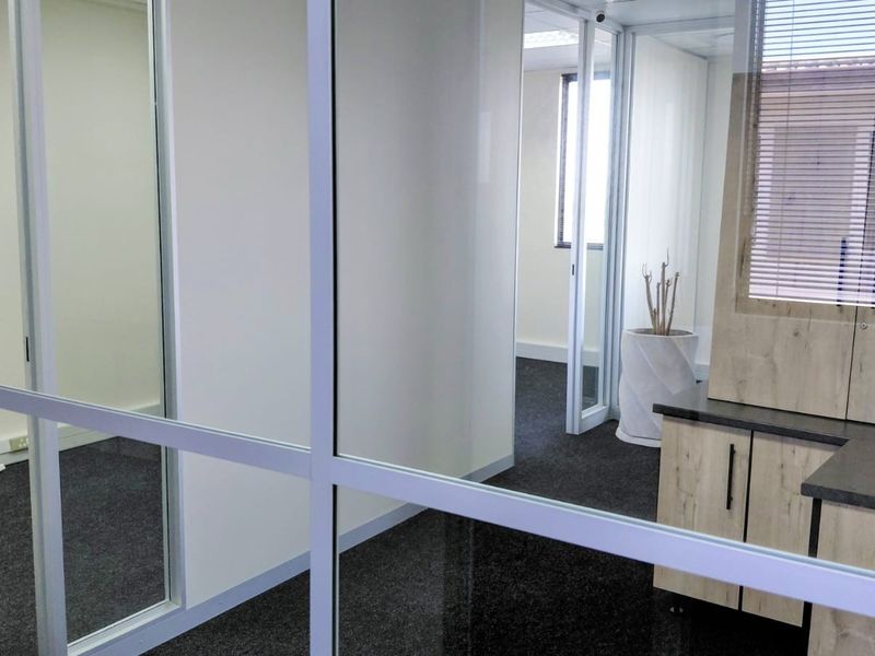 A modern office space featuring glass partitions, built-in cabinetry, and dark carpeting, offering a clean and professional environment for business operations.