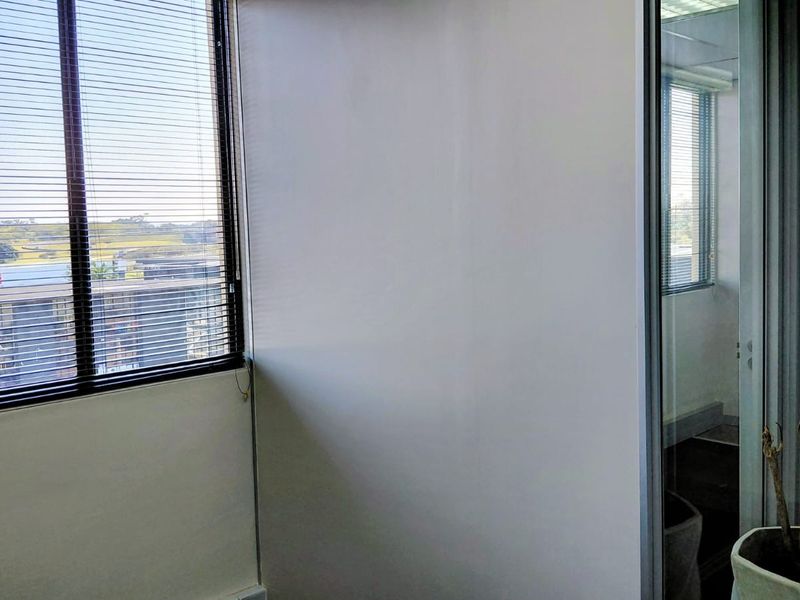 A bright, empty office space featuring large windows with venetian blinds and a modern glass partition, offering a clean and professional work environment.