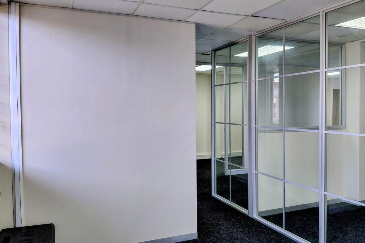 A vacant office space featuring glass partition walls, suspended ceilings with recessed lighting, and dark carpeting, offering a clean and professional layout.